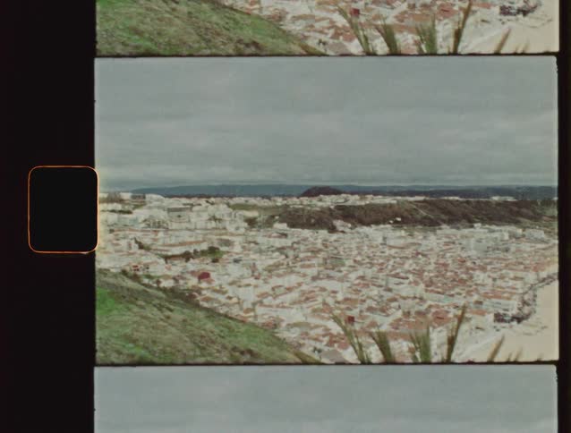 Vintage 8mm film reveals a panoramic view of the coastal city of Nazaré in Portugal, with its traditional houses and wide sandy beach