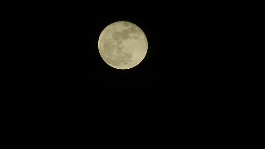 A beautiful time-lapse of a large full moon rising diagonally across a pitch-black night sky