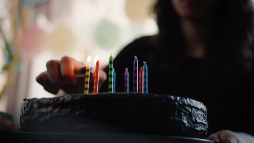 A woman lights colorful candles on a chocolate birthday cake in slow motion