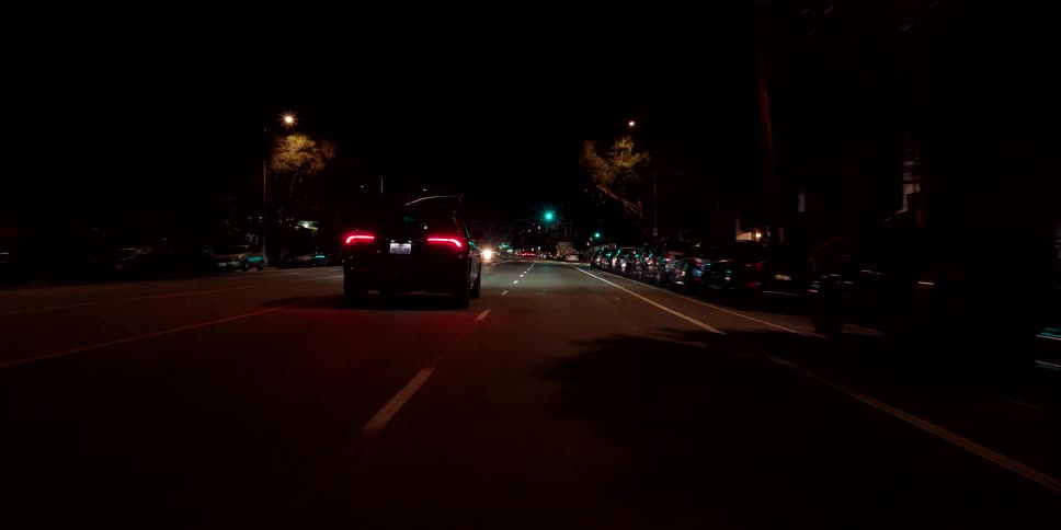Driving behind a sleek black luxury SUV as it cruises down a city street in the dark of night