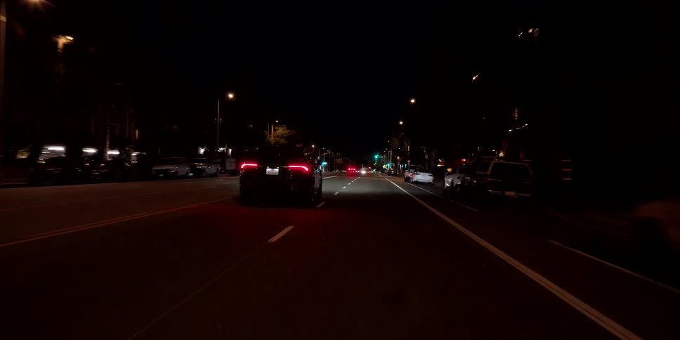 A point-of-view shot follows a sleek black car driving down a dimly lit city street late at night