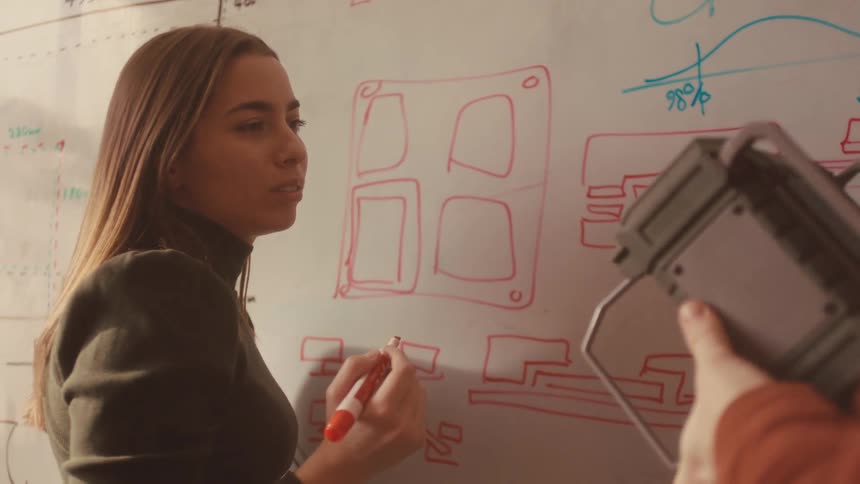 Focused female designer sketches a new product idea on a whiteboard while brainstorming with her male colleague in slow motion
