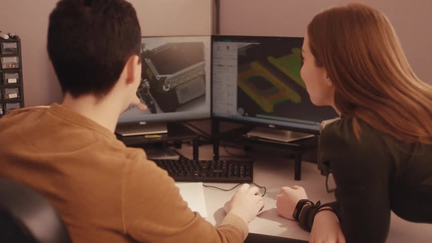 Two engineers collaborate on a 3D product design using CAD software, then examine the physical prototype together in their workshop