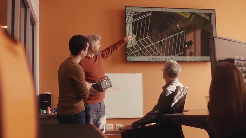 Three male engineers collaborate on a new product design, comparing a physical prototype to a 3D model on a screen in their modern office