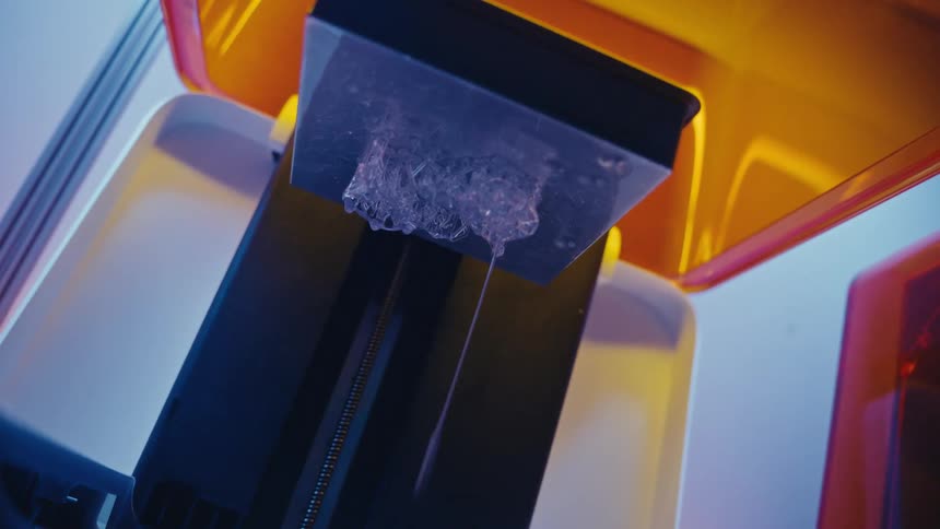 A newly created transparent object drips excess resin from the build plate of a modern 3D printer