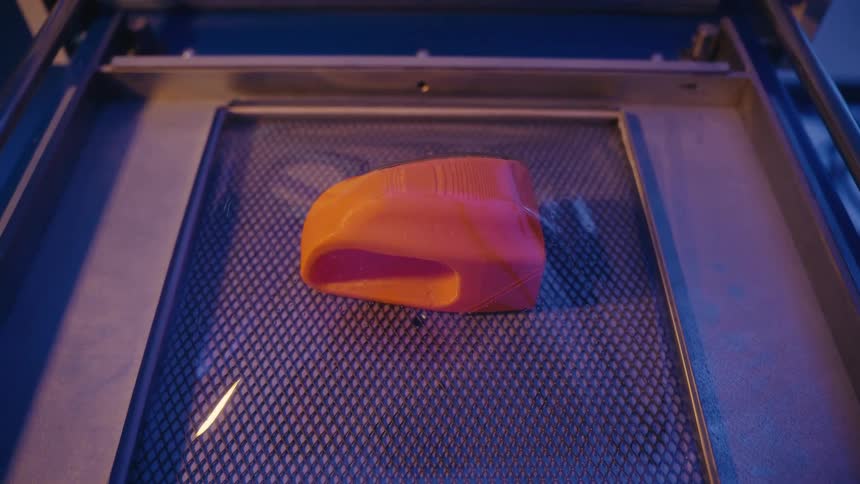A vacuum forming machine creates a clear plastic shell over an orange mold, which is then popped with a needle