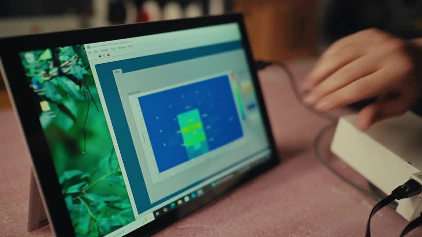 A technician tests a touch-sensitive surface, with a heat map on a tablet screen displaying the pressure points