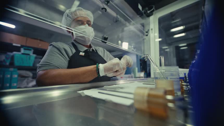 A laboratory technician in a face mask and gloves carefully prepares a specimen sample in a sterile environment