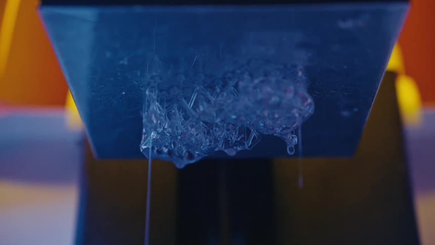 Close-up shot of a newly printed clear resin model with excess liquid dripping from the build plate of a 3D printer