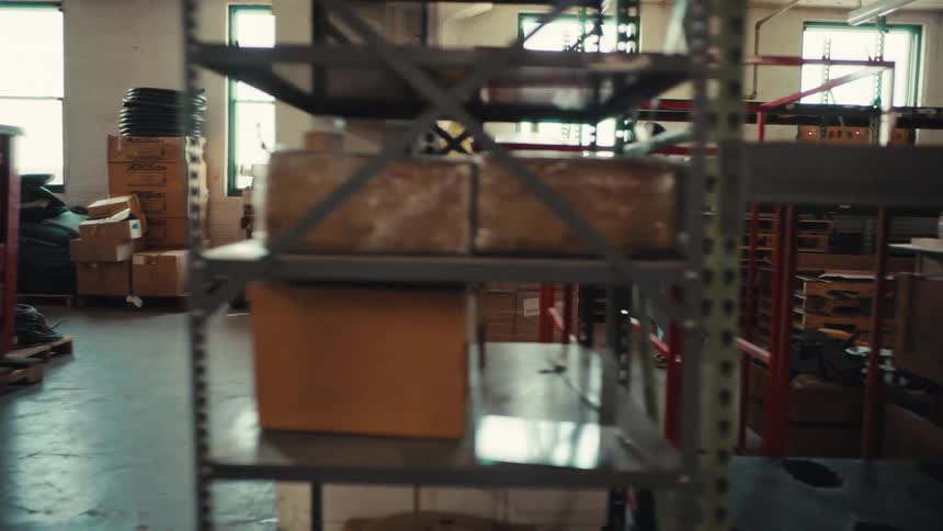 A warehouse worker uses a pallet jack to carefully move a large shipment of boxes through the aisles of an industrial facility