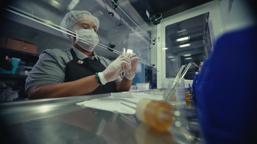 Slow motion focus pull to a masked and gloved worker carefully assembling a small component in a sterile lab