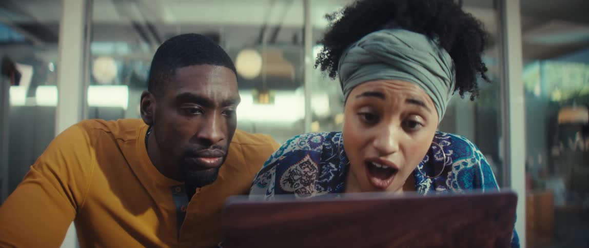 A young couple's expressions change from focused to surprised and excited while looking at a laptop screen together
