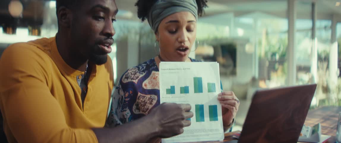 A young African-American man and woman discuss a bar chart while presenting business analytics during an online video conference