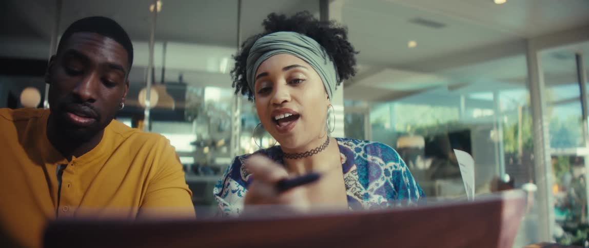 Two diverse young professionals collaborate on a project, reviewing documents and using a laptop in a bright, modern office
