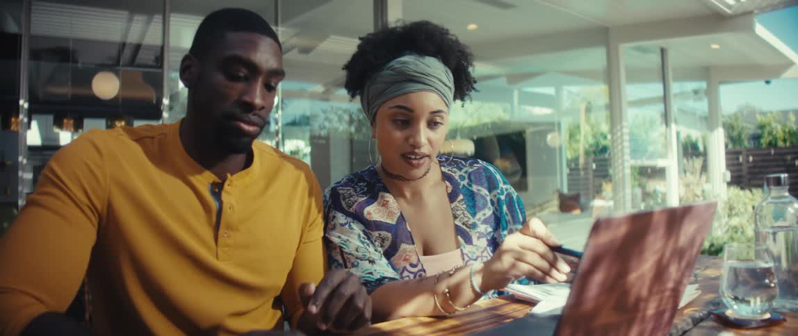 A focused young couple collaborates on their finances, using a laptop and calculator at a wooden table in their bright, modern home