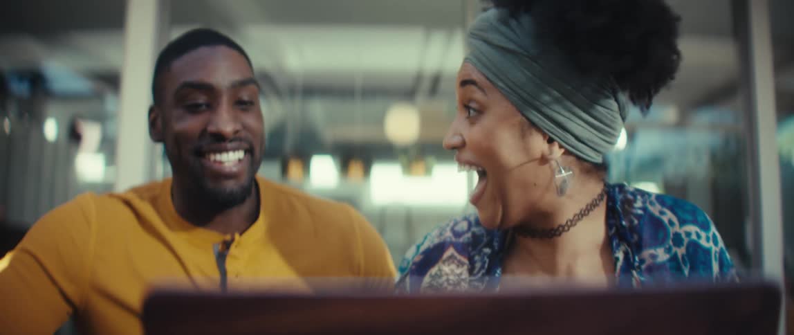 A young couple working on a laptop is overcome with surprise and joy, celebrating with an enthusiastic high-five