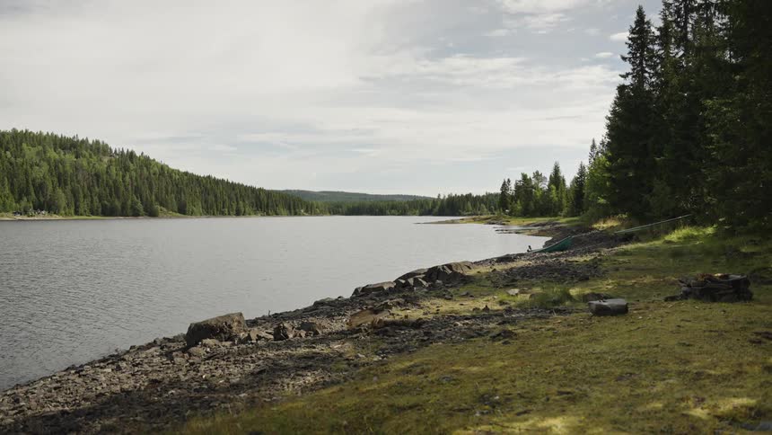 A tranquil view of a lakeside campsite with a rocky shore and dense forest on a calm day
