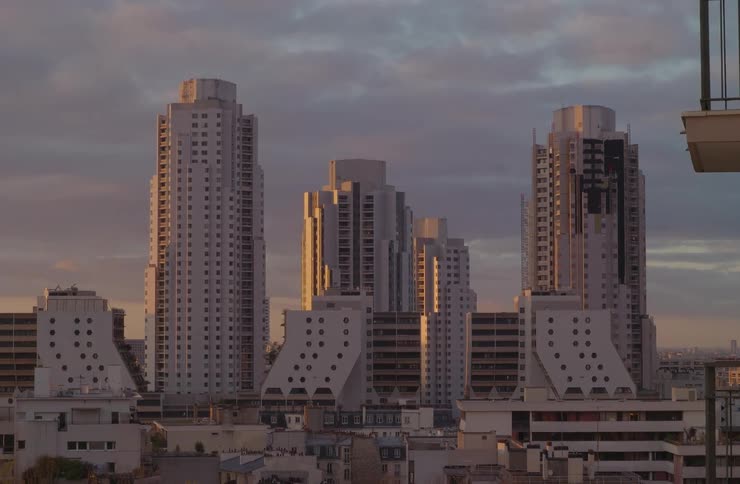 Modern city skyscrapers with unique architecture stand tall against a cloudy sky during a warm golden sunrise