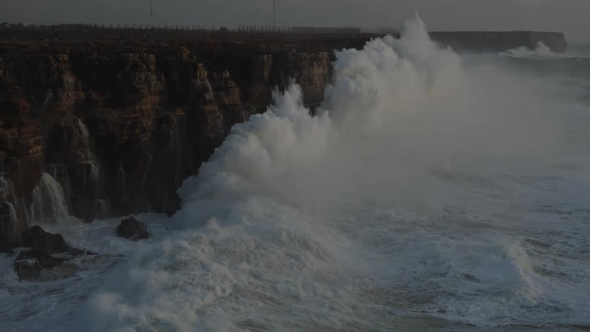 Massive ocean swells explode against a dramatic cliff face in slow motion