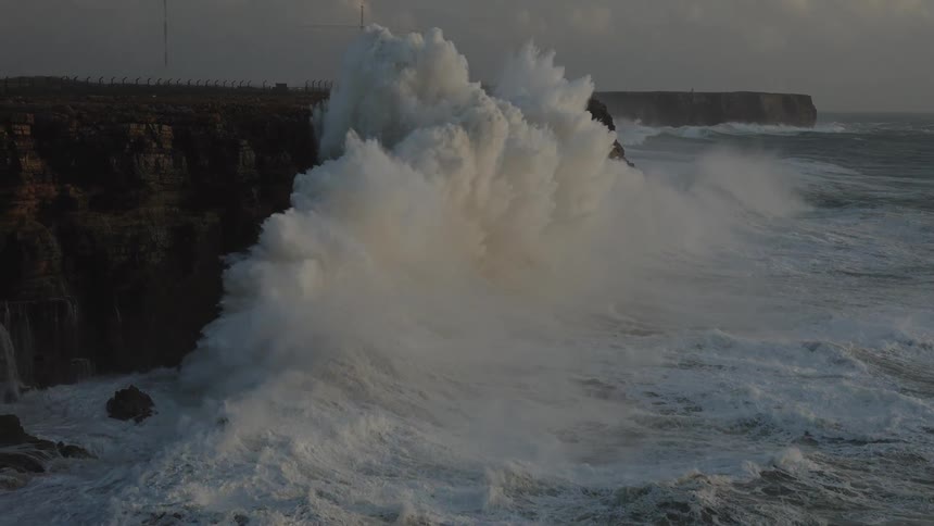 Dramatic slow motion shot of a colossal ocean wave exploding with force against a rugged cliff during a fierce storm