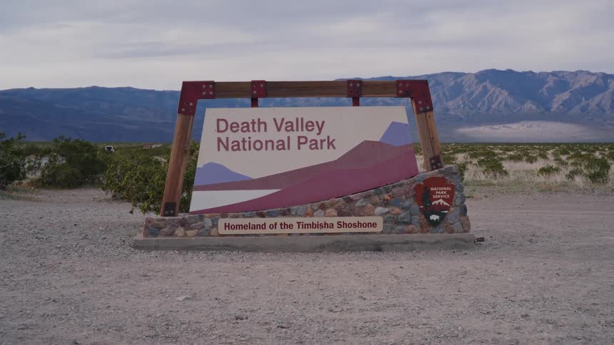 A dynamic dolly zoom shot captures the welcome sign to Death Valley National Park set against the vast desert and mountain landscape