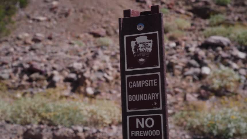 A stylized zoom-in shot focuses on a National Park Service sign marking a campsite boundary in a desert canyon