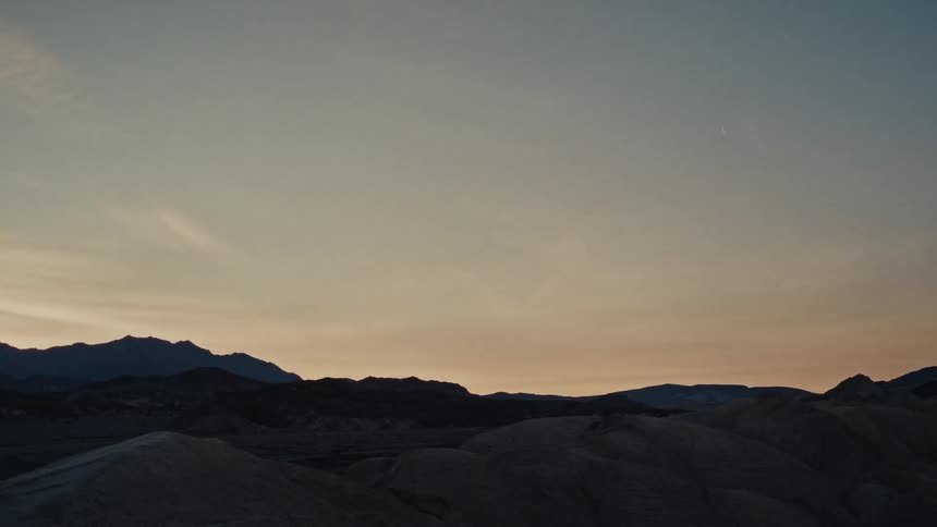 A stunning timelapse shows the sky transitioning from a dark, moonlit night to a warm, golden sunrise over a silhouetted desert mountain range