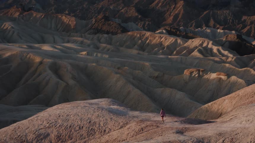 A lone woman explores the vast, rolling badlands of a desert landscape during a golden sunrise