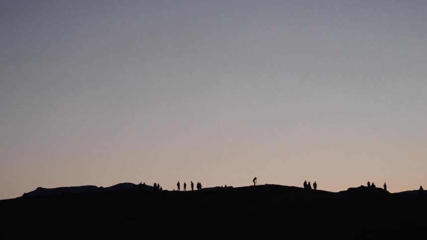 Silhouettes of people gathered on a hilltop against the serene gradient of a twilight sky