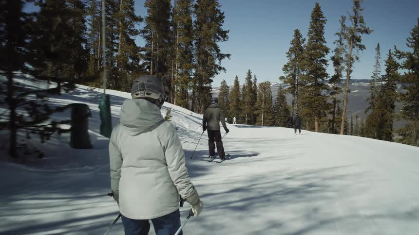 A slow-motion point-of-view shot follows a group of skiers down a groomed slope on a sunny day at a mountain resort