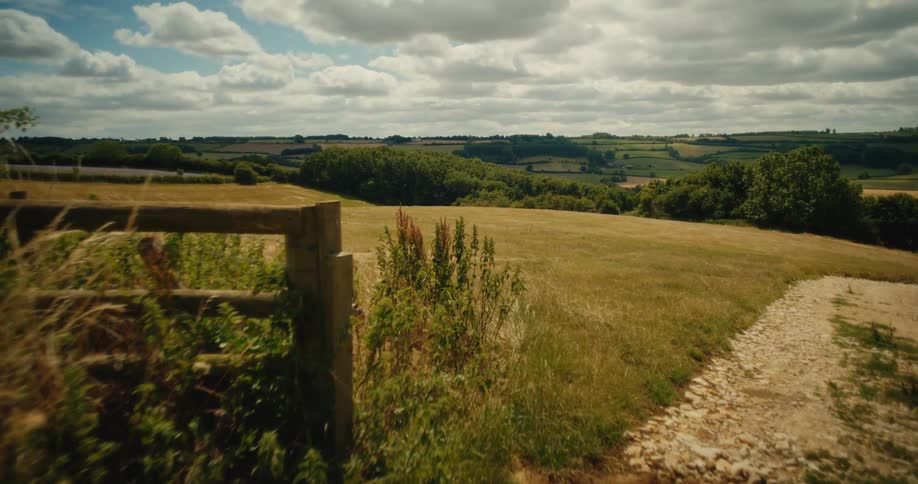 A slow push-in shot past a wooden fence reveals a beautiful view of the rolling hills in the English countryside on a summer day