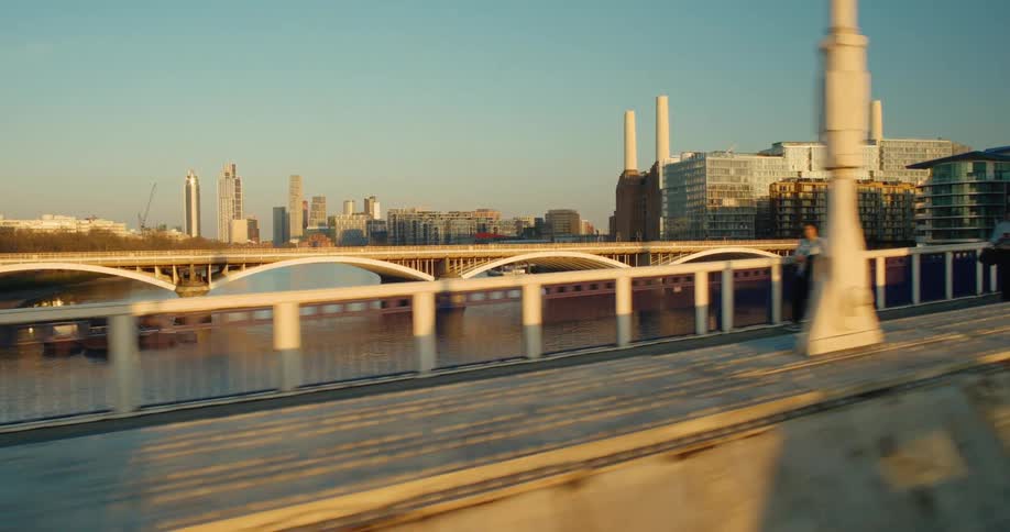 Scenic tracking shot over a London bridge revealing the Battersea Power Station and city skyline at golden hour
