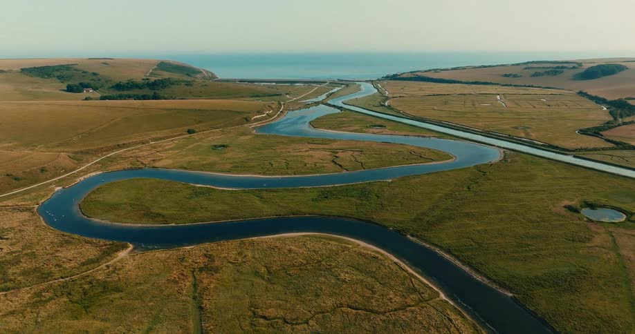 An aerial view of a serpentine river winding through lush green marshlands and fields towards the distant ocean