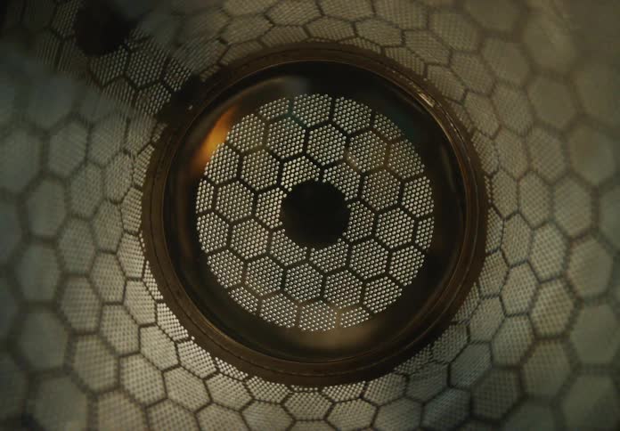 An abstract close-up shot slowly pulls back from a circular metallic object featuring an intricate honeycomb pattern
