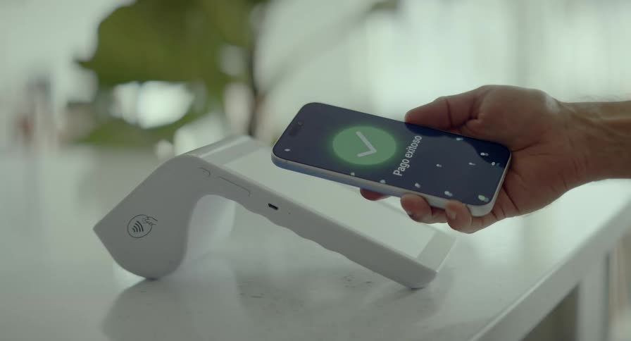 A man completes a successful contactless payment in Spanish by tapping his smartphone on a white POS terminal