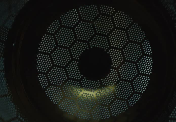 A close-up of a metallic hexagonal grid with flashing light reflecting off its surface