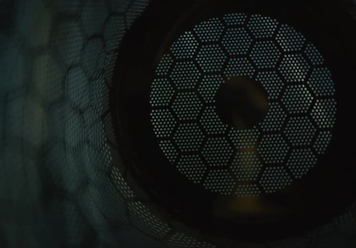 An abstract, mesmerizing view down a dark tube with a honeycomb pattern as light shifts across its surface