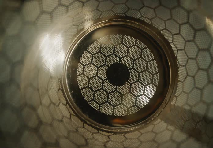 Shifting light illuminates a futuristic metallic honeycomb mesh filter creating hypnotic patterns