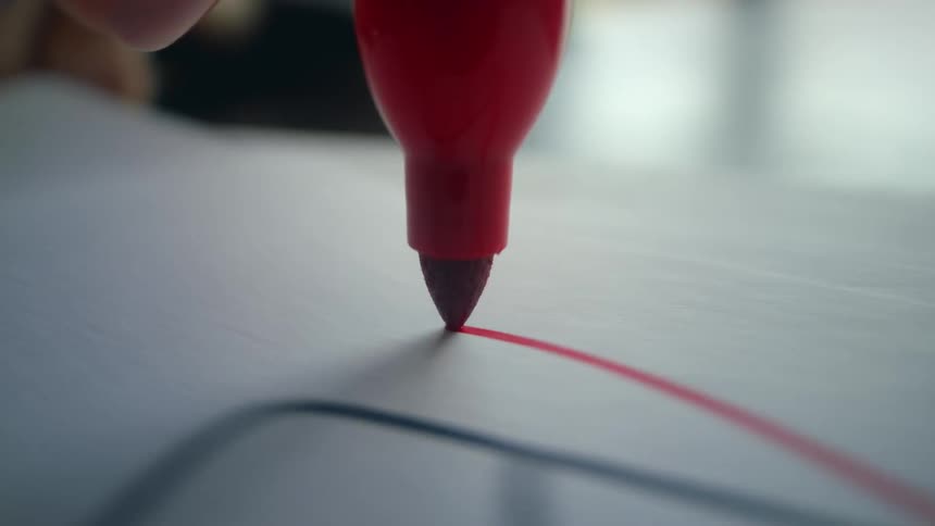 Extreme close-up of a red marker's felt tip as it draws lines and circles on a white surface
