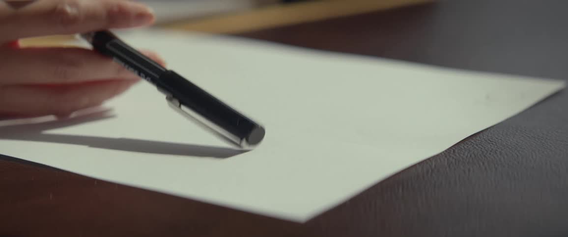 A close-up slow-motion shot of a hand nervously tapping a pen over a blank piece of paper