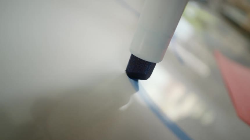 An extreme close-up shot follows a blue marker as it draws lines and diagrams on a reflective whiteboard