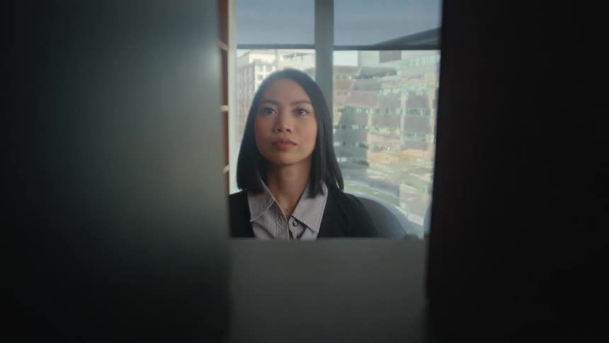 View from inside a bookshelf as a woman places a large book on the shelf, blocking the camera in a modern city office