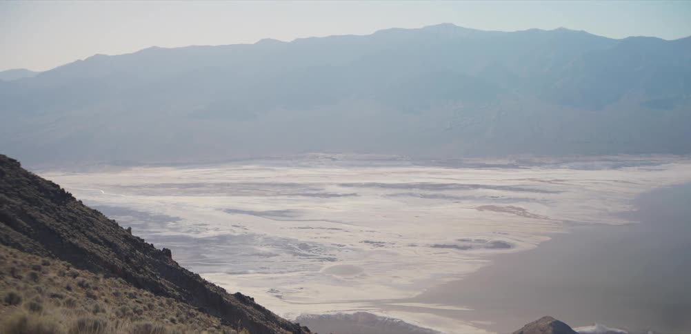 A breathtaking, hazy panoramic view of a vast desert valley floor from a high mountain overlook
