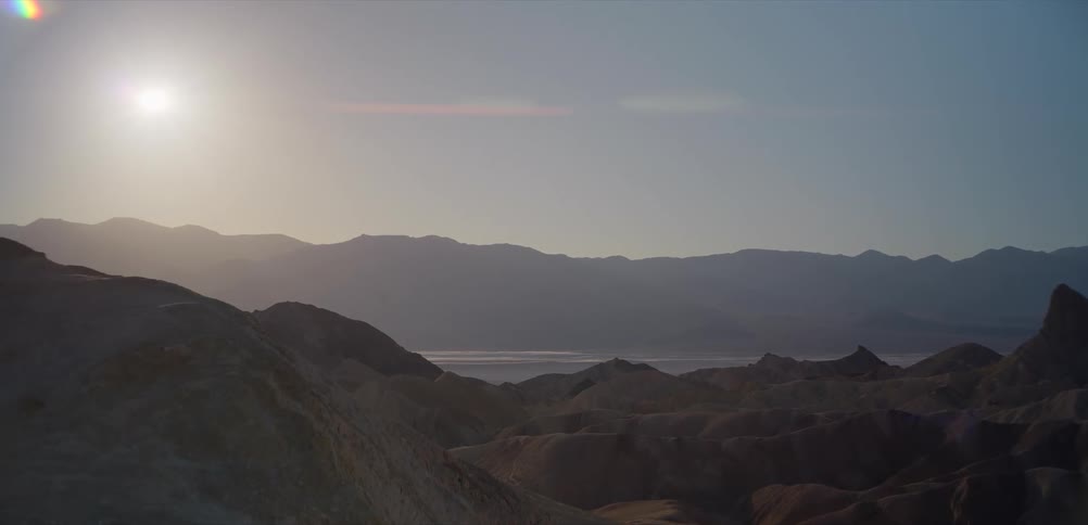 A serene, static shot of the sun setting over a vast and hazy desert mountain landscape in Death Valley