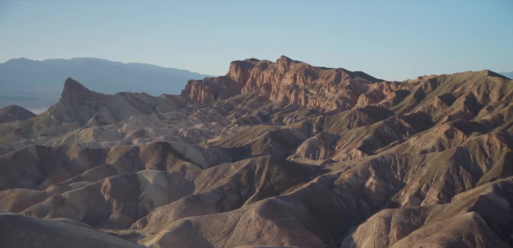A static shot of the rugged, eroded badlands of Zabriskie Point in Death Valley National Park under a clear blue sky
