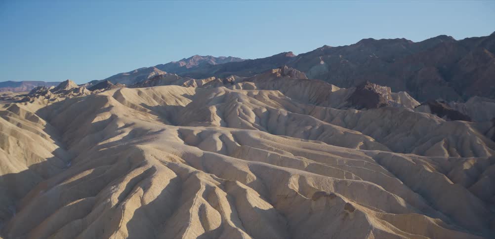 Golden sunrise light casts long shadows across the vast, eroded badlands of Zabriskie Point in Death Valley National Park