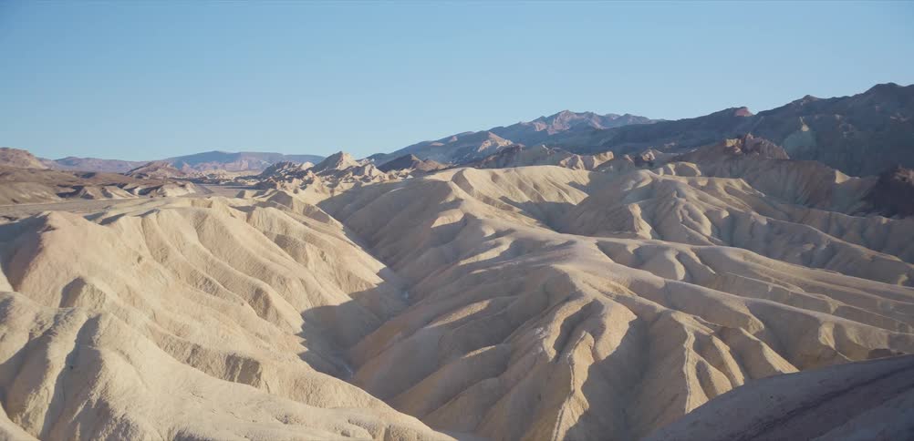 A slow zoom out reveals the expansive, sunlit badlands of a desert landscape at sunrise