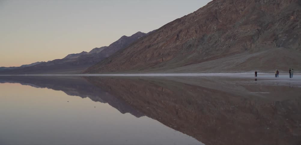 A tranquil and serene shot of a desert mountain range perfectly reflected in the still, glassy water of a vast salt flat at dawn