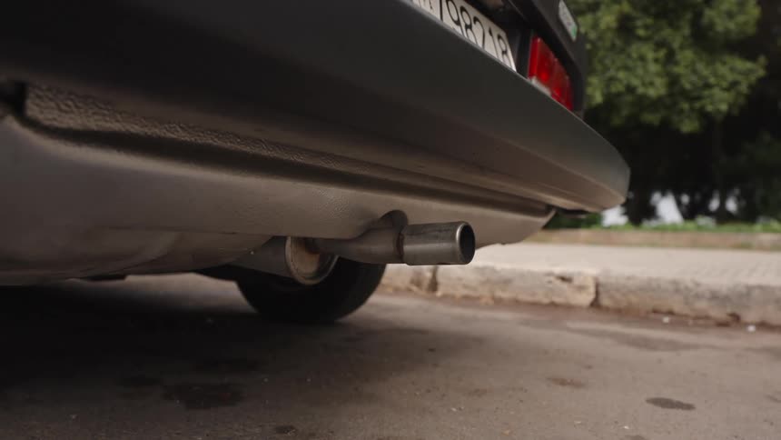 Low-angle close-up of a car's exhaust pipe as the engine idles on an asphalt road