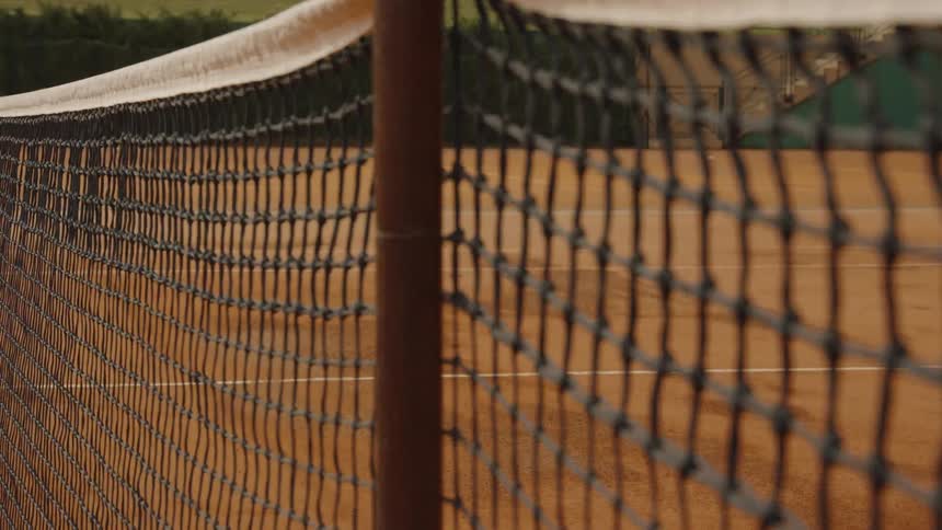 A close-up shot of a tennis net on a clay court as the focus slowly shifts